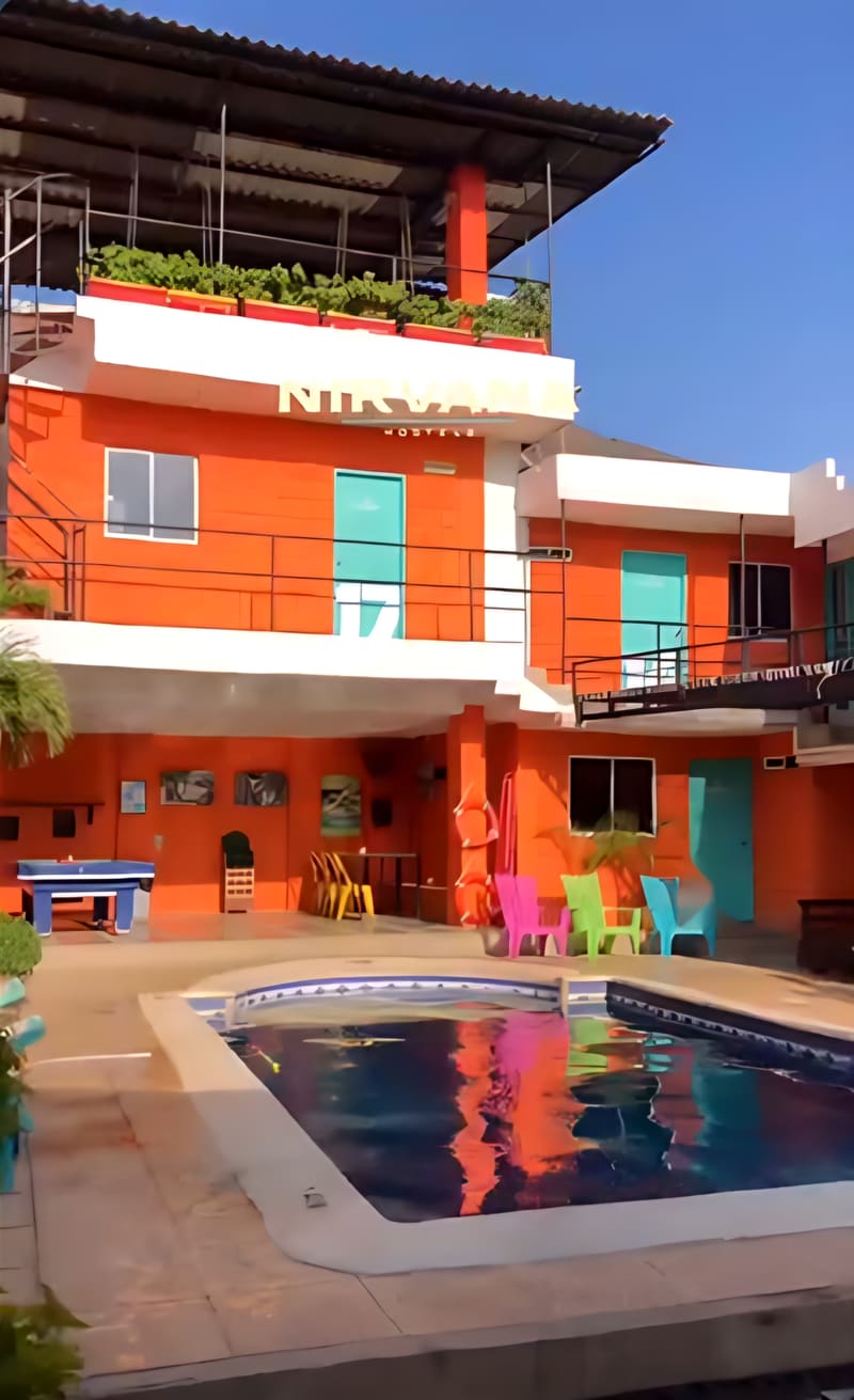 La fachada naranja del hostal con el letrero Nirvana Hostels, la piscina en primer plano y la mesa de billar al fondo.