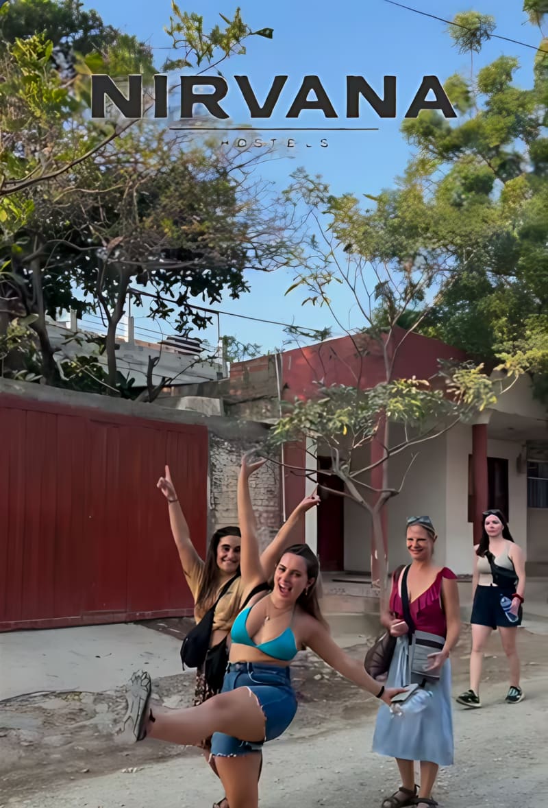 Cuatro viajeras posan y ríen en la calle de tierra frente al portón del hostal.
